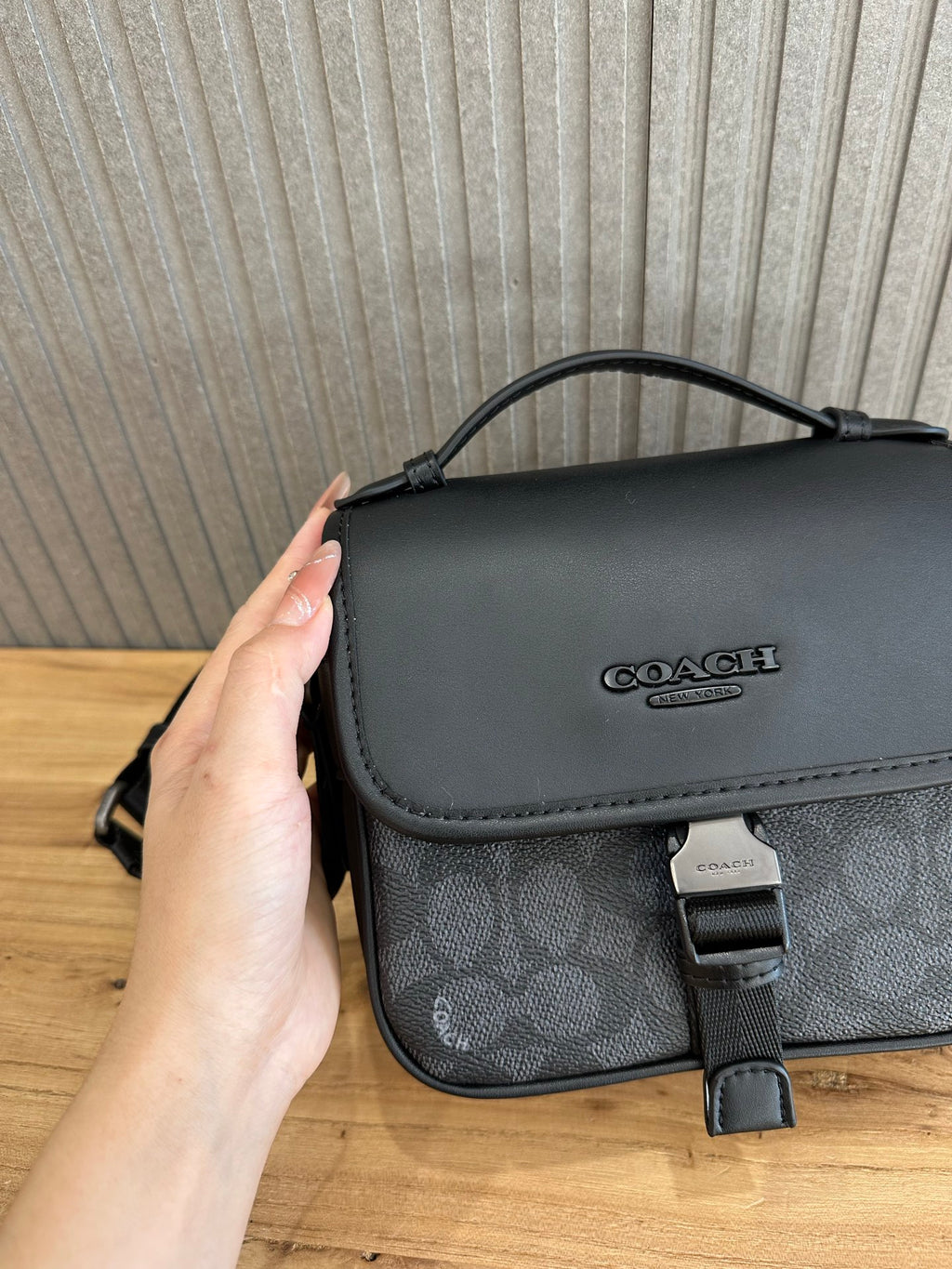 Coah crossbody bag close-up; black flap with emblem, patterned front panel, top handle strap