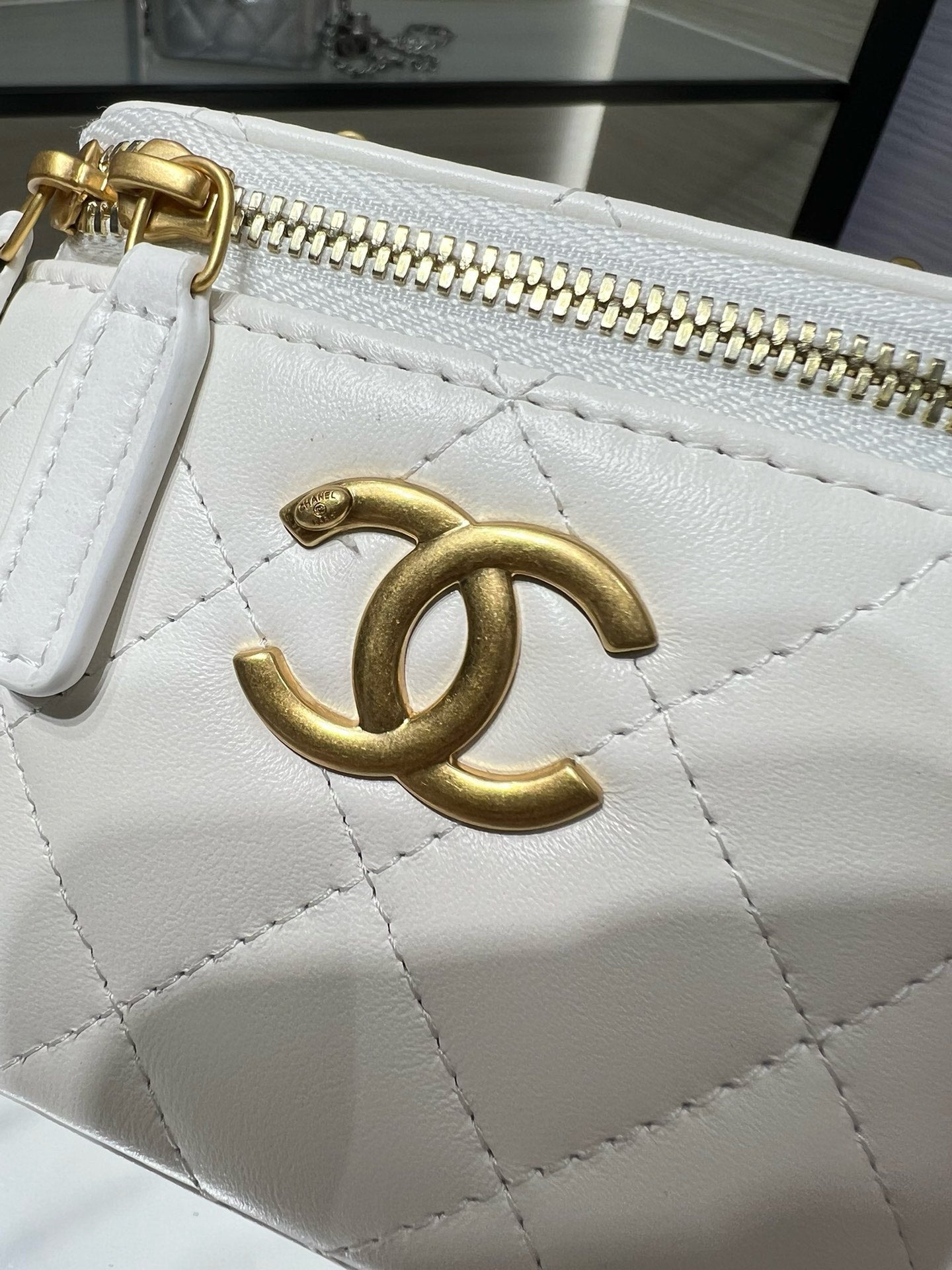 White quilted mini bag close-up with gold CC emblem and gold-tone zipper hardware.