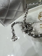 Silver chain strap with interlocking charms beside small silver flap bag