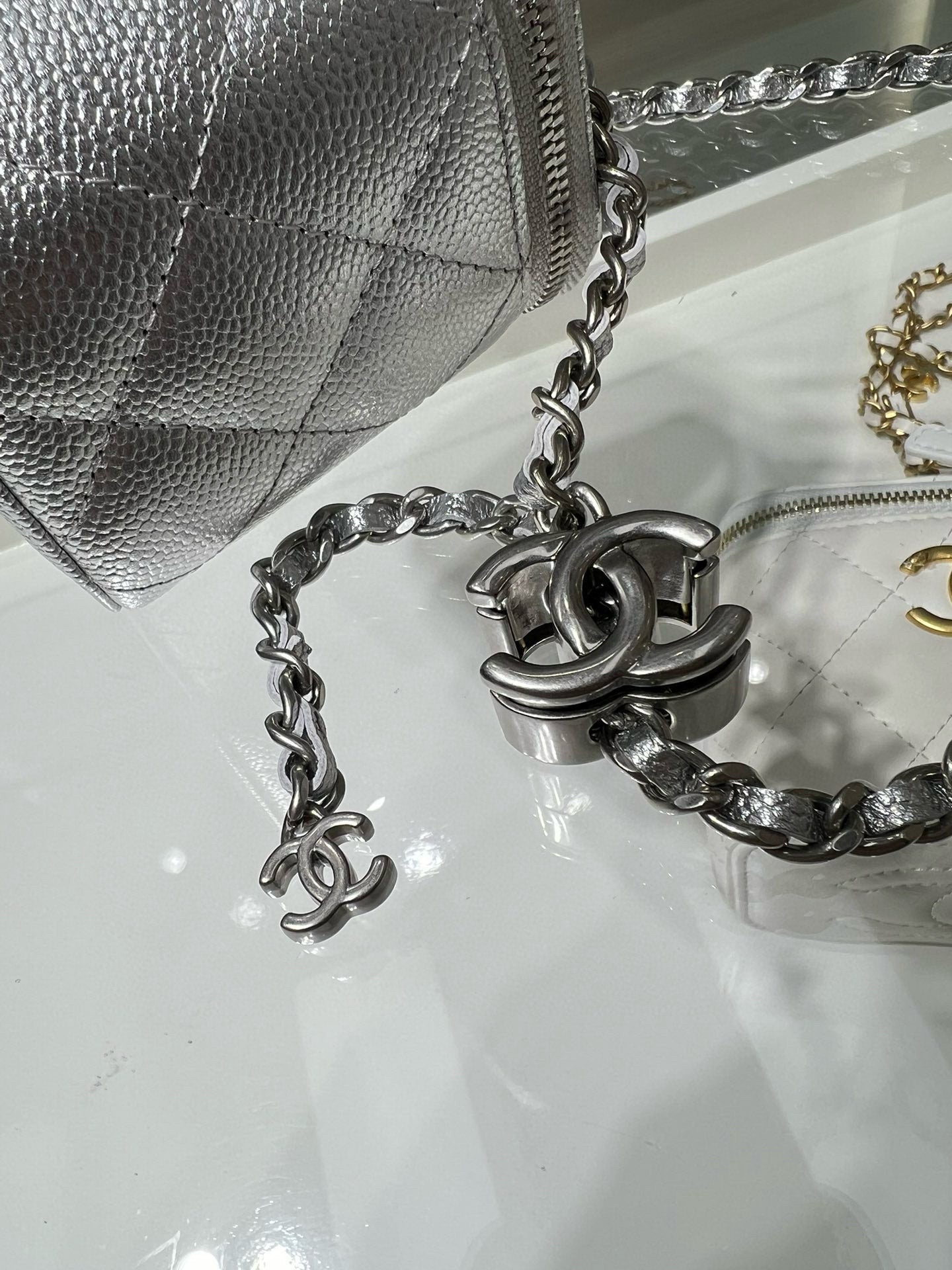 Silver chain strap with interlocking charms beside small silver flap bag