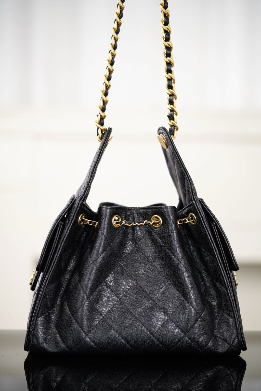 Black Chanel quilted bucket bag with two gold chain straps and top handle tabs