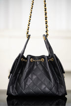 Black Chanel quilted bucket bag with two gold chain straps and top handle tabs