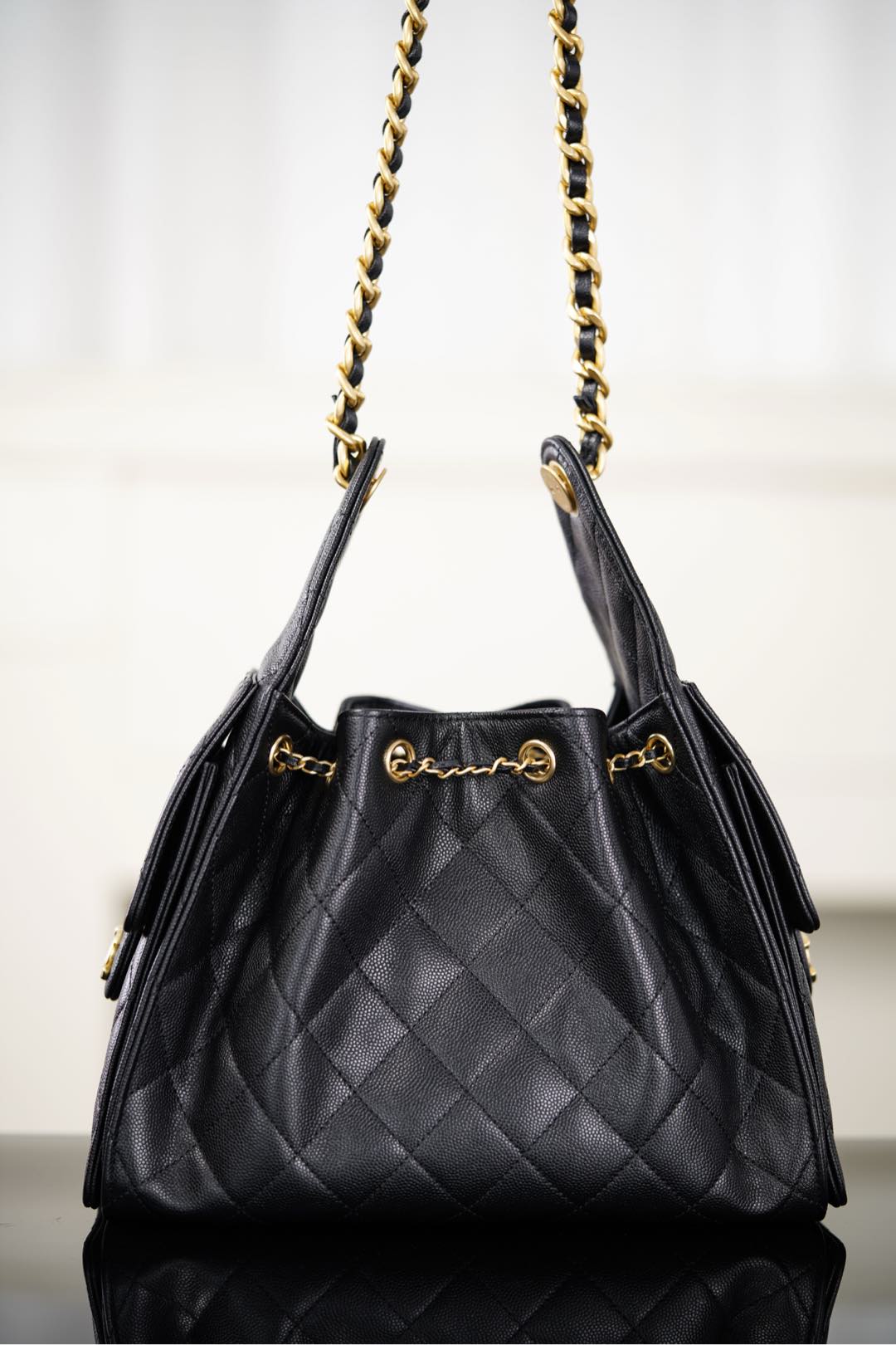 Black Chanel quilted bucket bag with two gold chain straps and top handle tabs