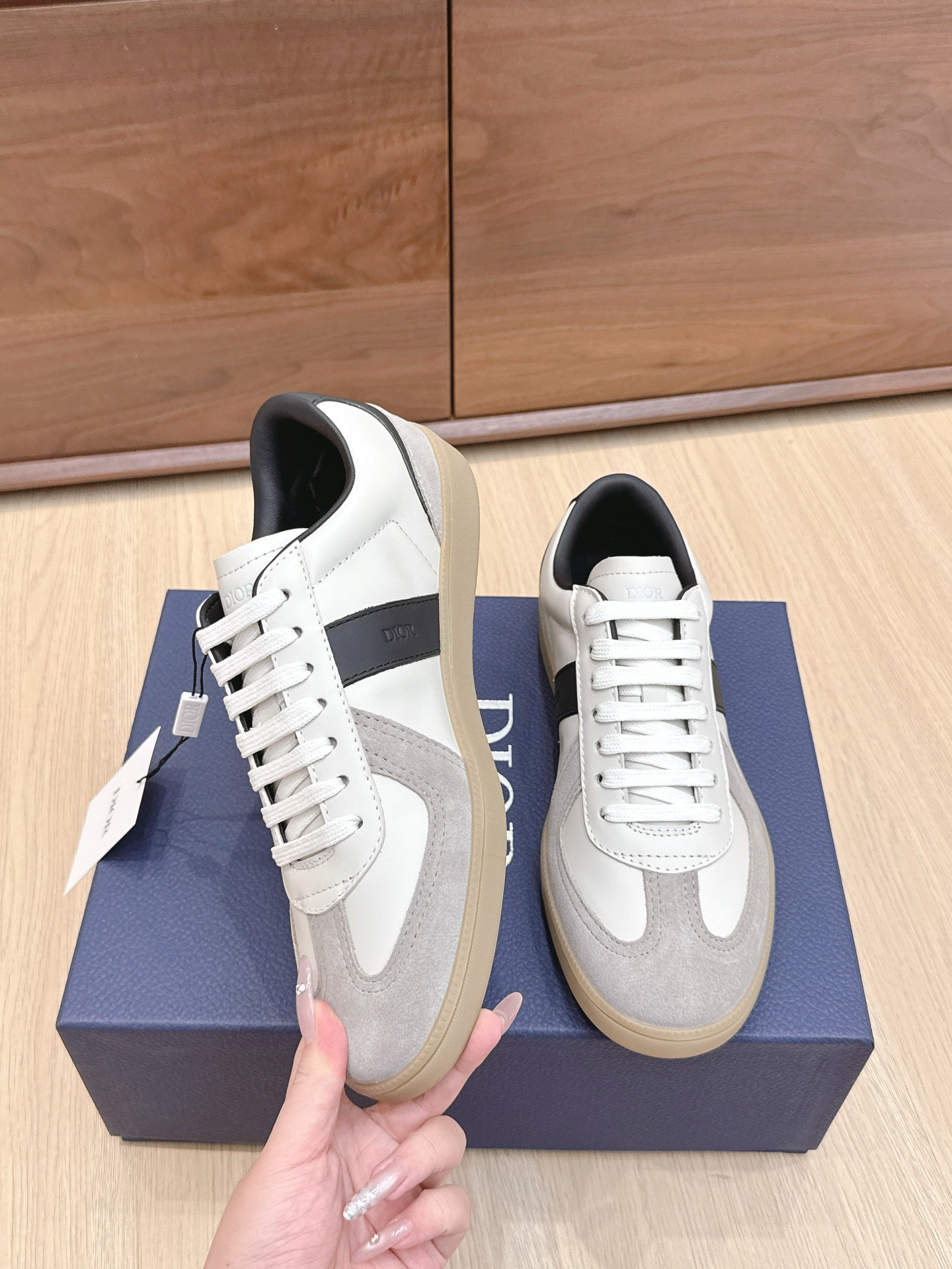 White and gray lace-up sneakers with black heel, held above a blue shoebox.