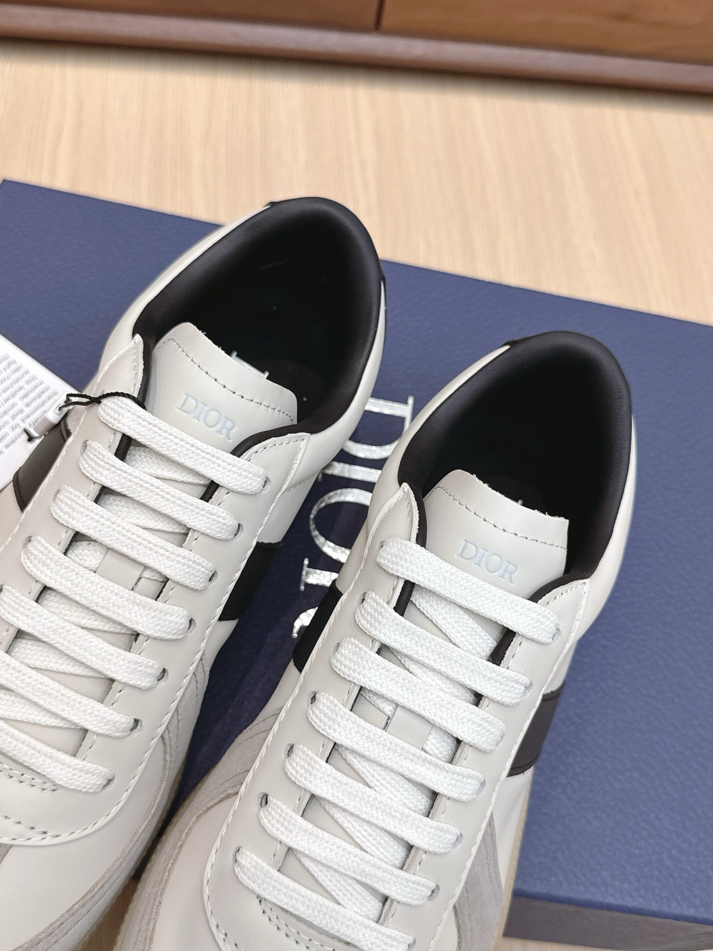 Two white lace-up sneakers with black lining and “Dior” label inside heel.