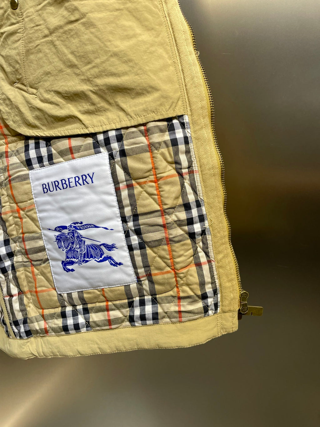 Plaid-lined Burberry pocket detail with blue horse graphic and yellow jacket trim.