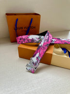 Louis Vuitton belt with pink floral canvas strap and silver LV buckle, resting end.
