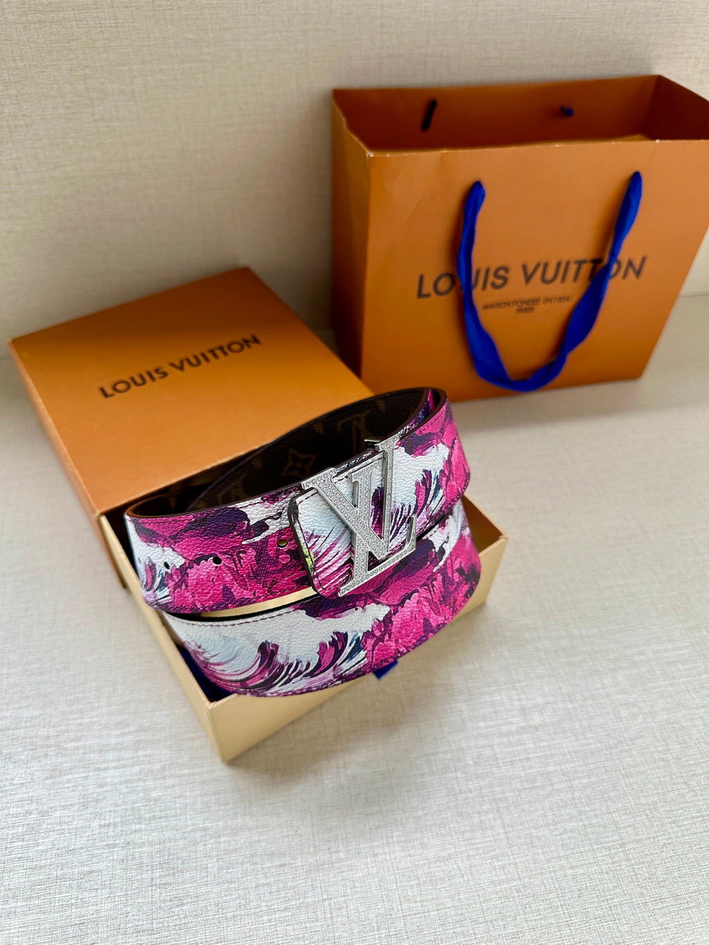 Louis Vuitton belt with pink floral canvas strap and silver LV buckle, laid flat.