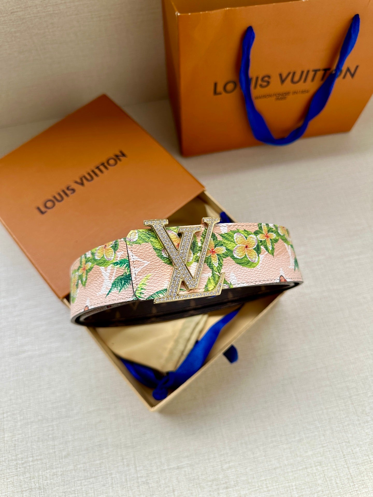 Louis Vuitton belt showing silver LV buckle on pink floral strap with green tropical flowers