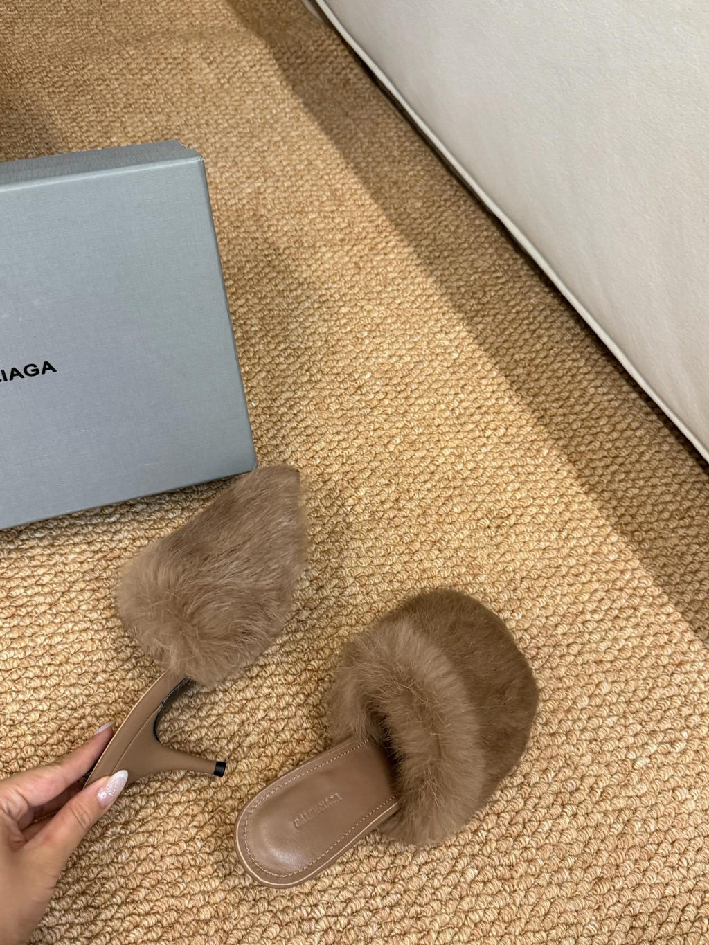 Taupe faux-fur slide sandals held in hand; low heel and tan sole visible
