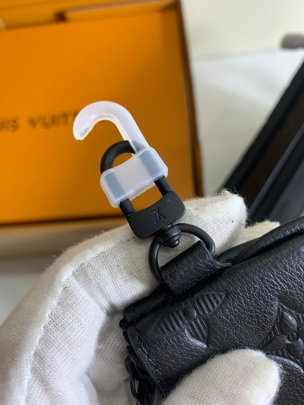 Louis Vuitton bag hardware with strap and key clasp attached to dark leather accessory