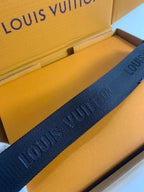 Louis Vuitton crossbody strap in dark textured woven fabric with repeating pattern.