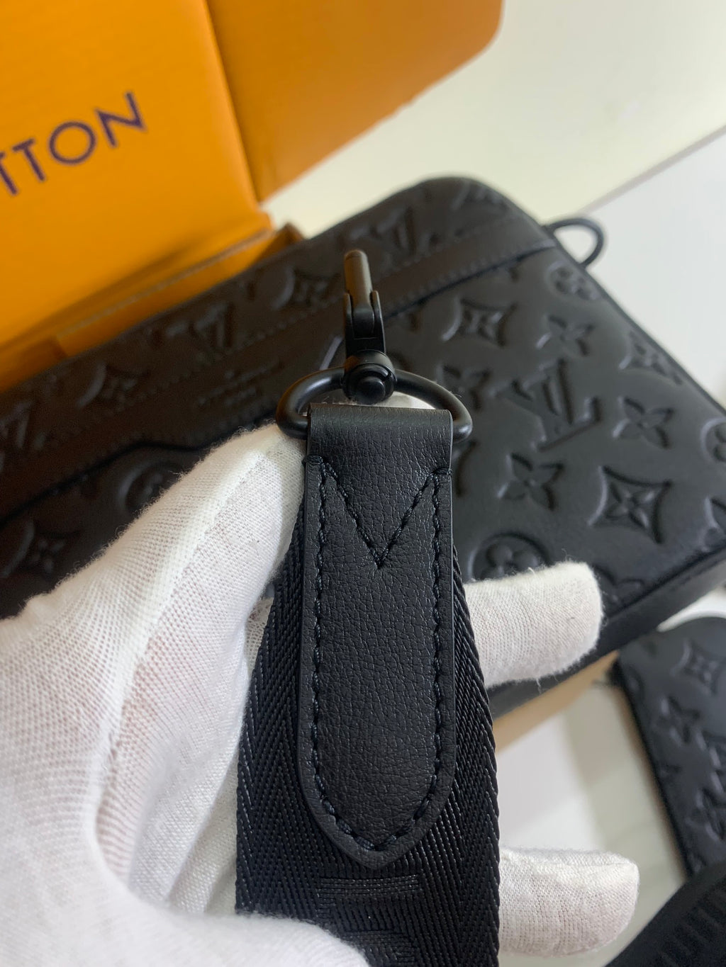 Louis Vuitton crossbody bag detail: dark monogram leather top zipper pull and leather tab.