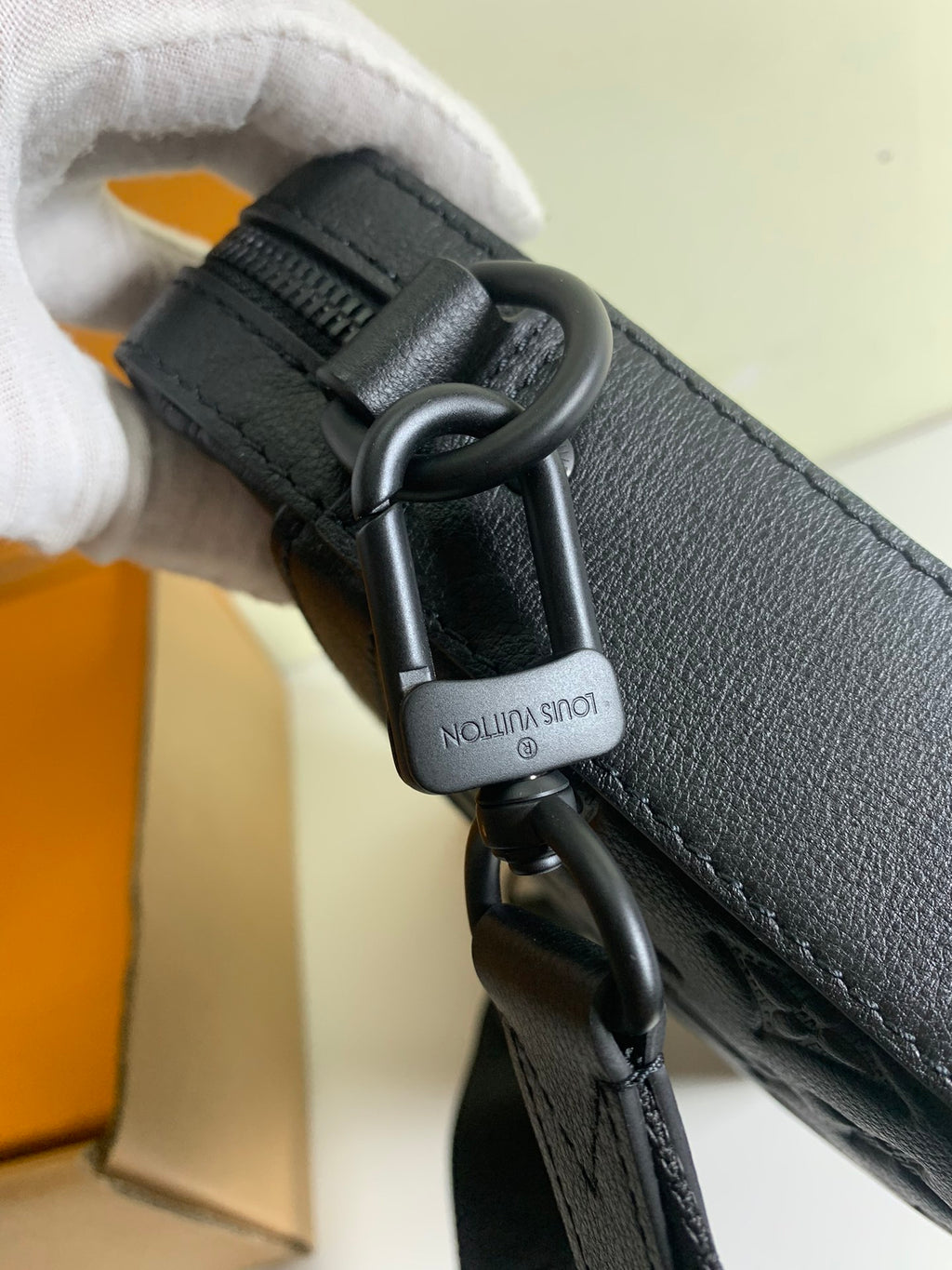 Louis Vuitton strap clasp with 'Louis Vuitton' text on dark leather, metal hardware