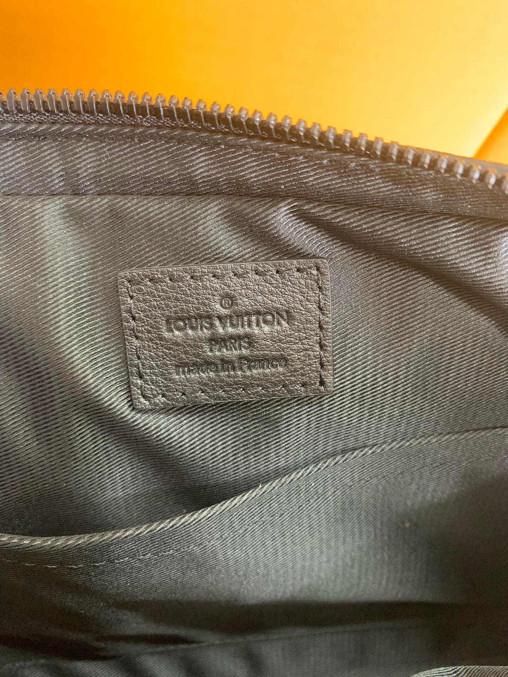 Louis Vuitton bag interior label on dark fabric lining beneath the zipper seam.
