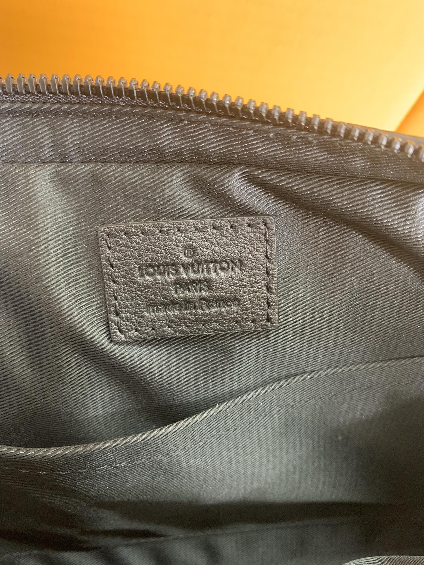 Louis Vuitton bag interior label on dark fabric lining beneath the zipper seam.