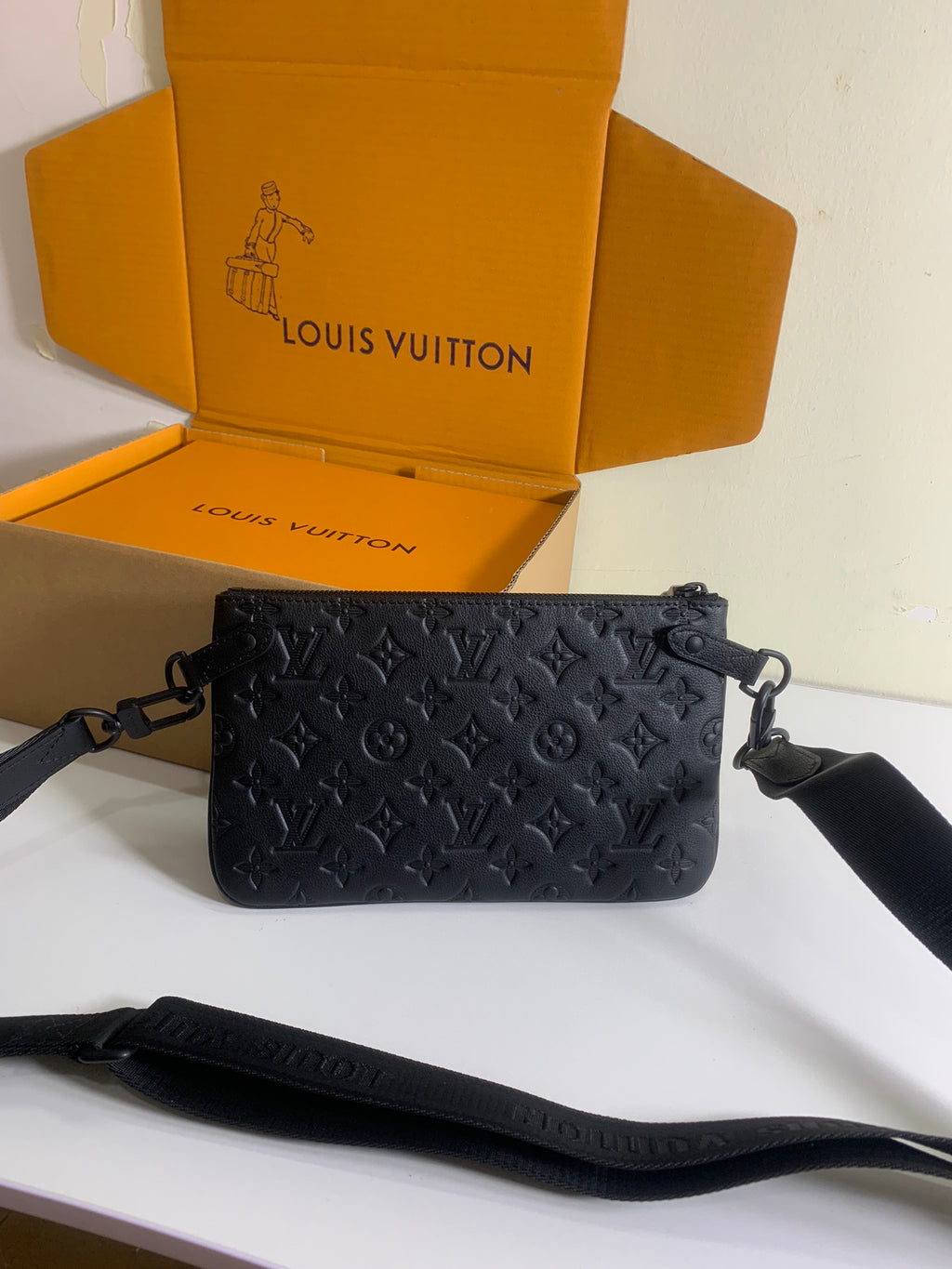 Louis Vuitton crossbody bag with dark embossed monogram print, side straps, and short handle.