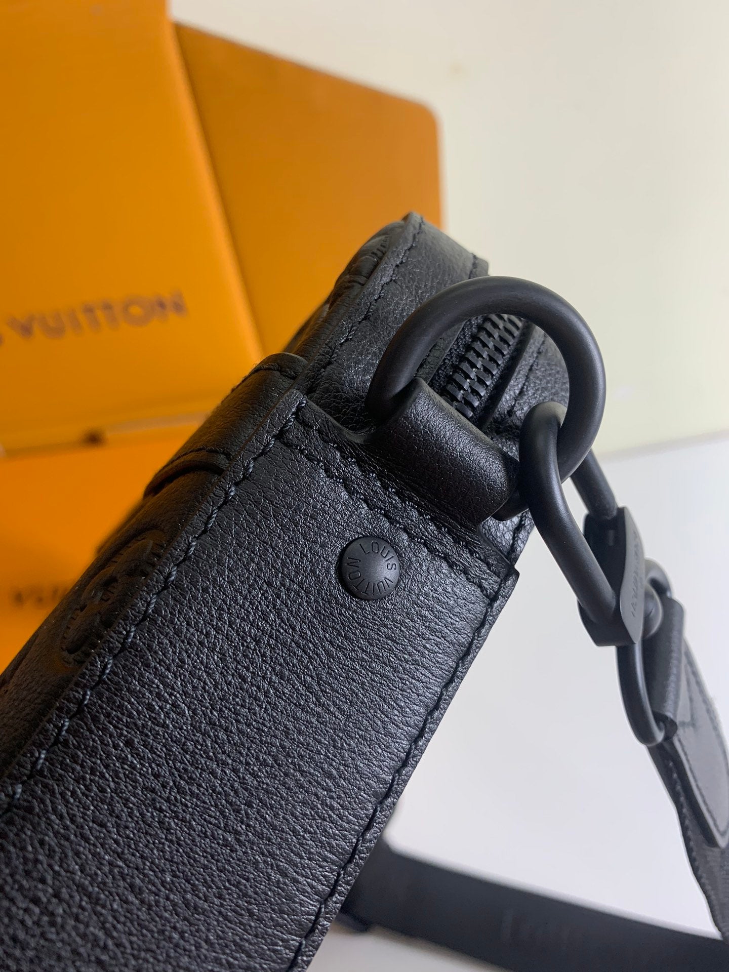 Louis Vuitton bag in dark monogram leather with textured strap and metal ring attachment.
