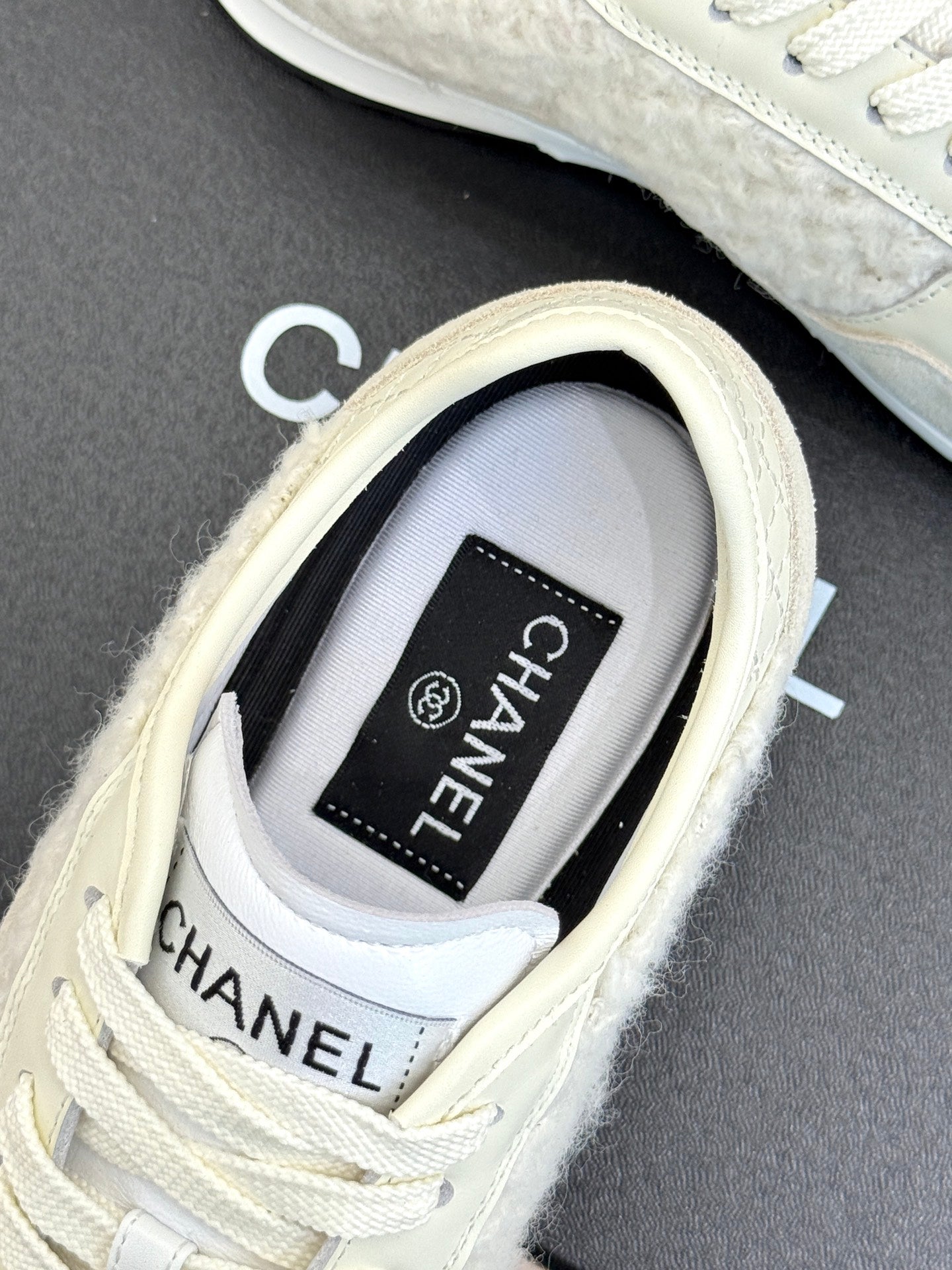 White Chanel sneakers close-up, CHANEL logo patch on tongue