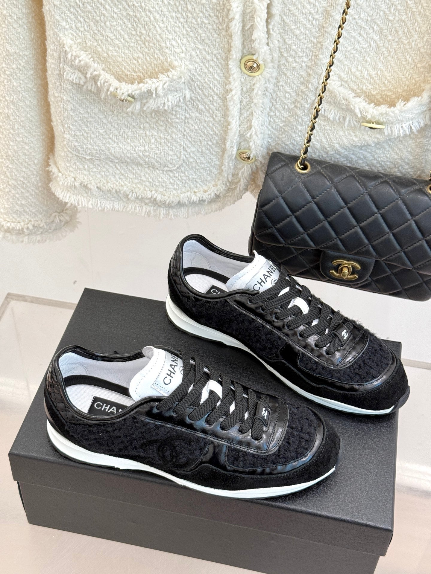 Pair of Chanel black sneakers with white trim, side-by-side on shoe boxes