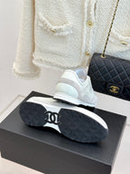 White Chanel sneakers on black shoebox, with black quilted handbag