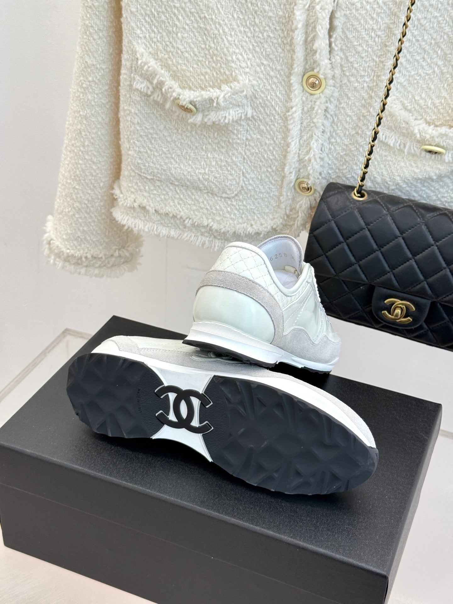 White Chanel sneakers on black shoebox, with black quilted handbag