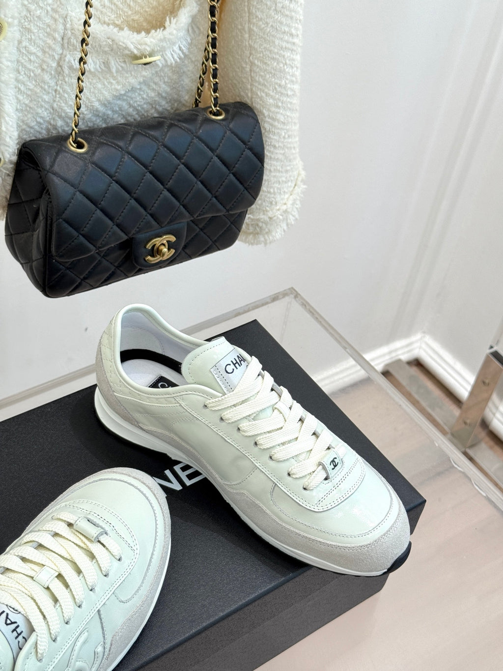 White Chanel sneakers with lace-up design beside black quilted handbag