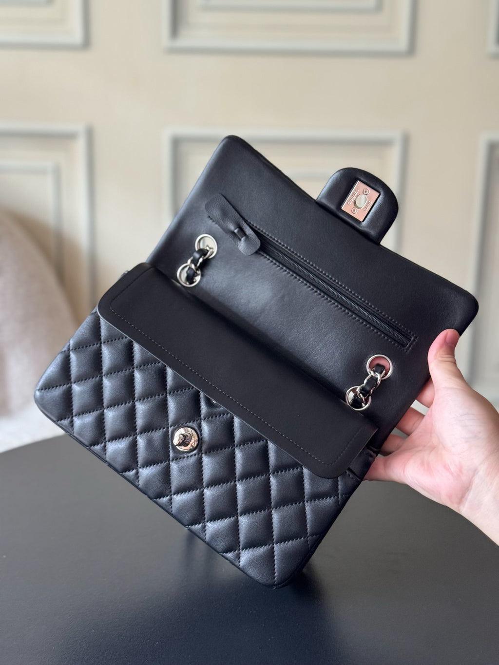 Black quilted Chanel shoulder bag held in hand with chain strap and front flap.