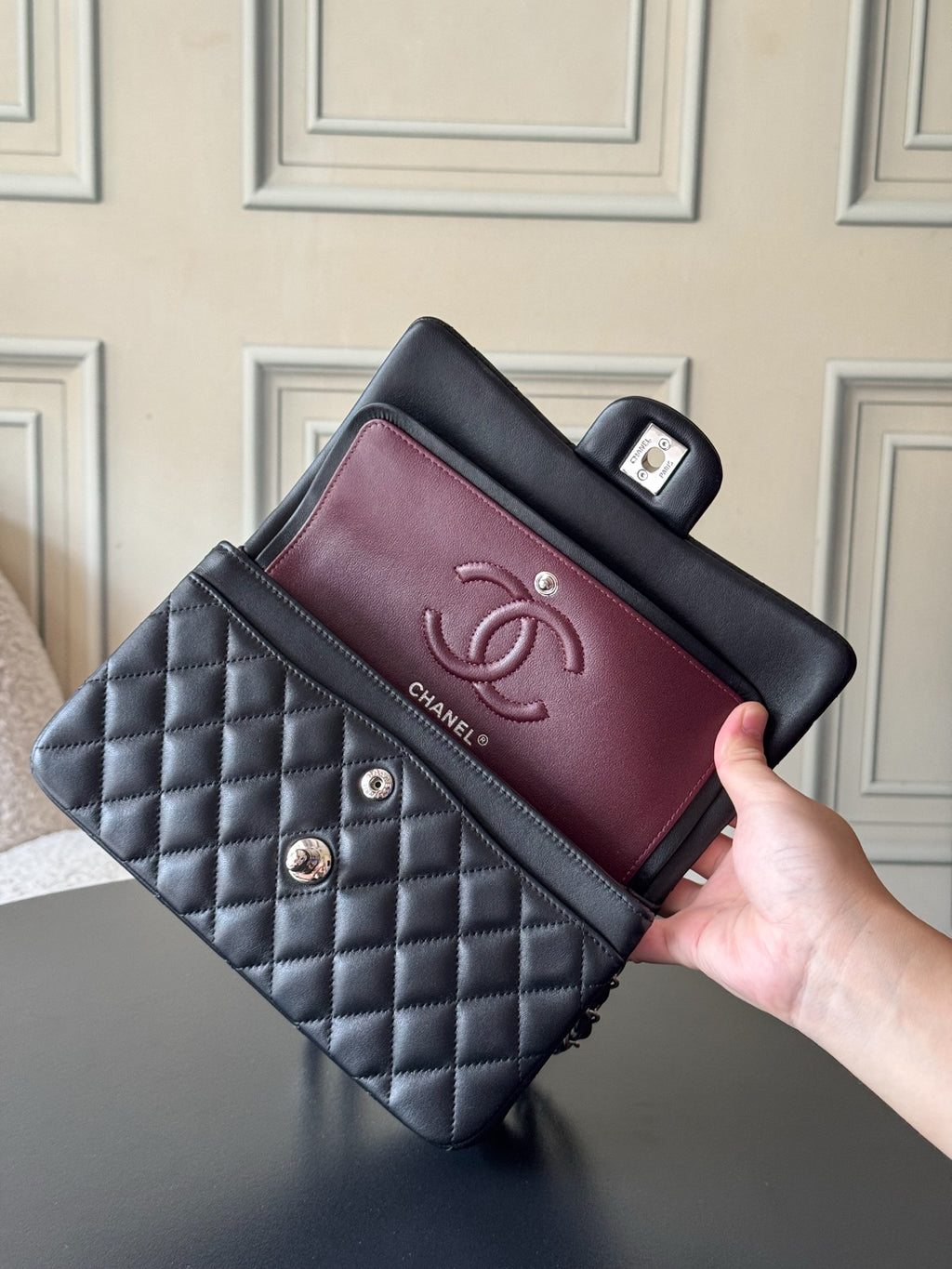 Black quilted Chanel bag with burgundy interior flap and CC logo, held up to view.