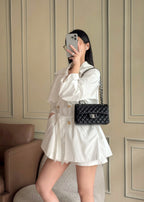 Black quilted Chanel crossbody bag with chain strap worn on a white dress.