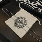Chrome Accessories necklace with round pendant draped over fabric pouch in box.