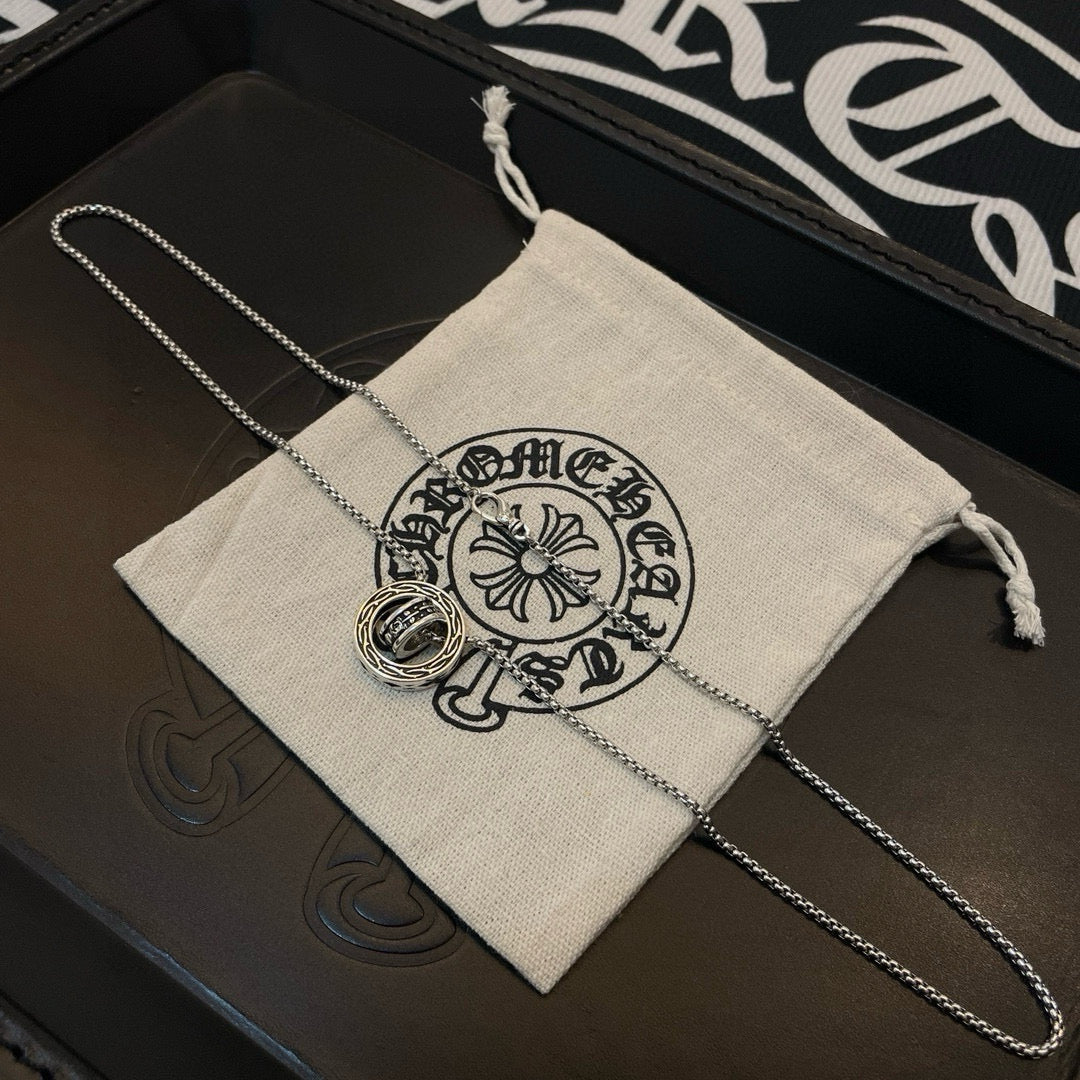 Chrome Accessories necklace with round pendant draped over fabric pouch in box.