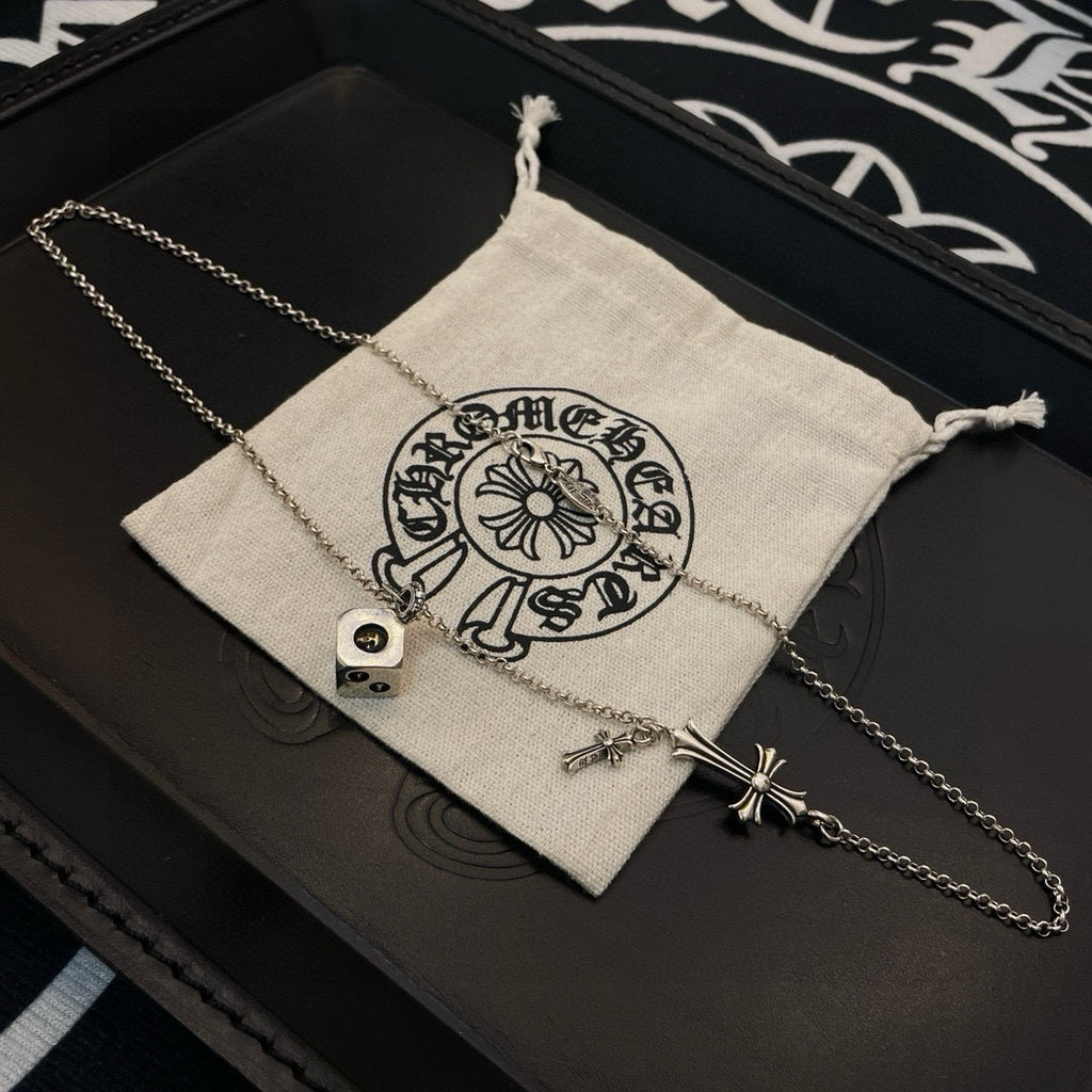 Silver charm necklace with cross pendant, laid across a fabric pouch in a box
