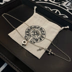 Silver charm necklace with cross pendant, laid across a fabric pouch in a box