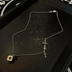 Silver cross charm necklace with square coin pendant on a black embossed tray