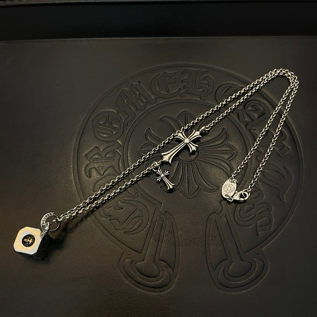 Silver charm necklace with cross and heart tag pendant, flat on black surface