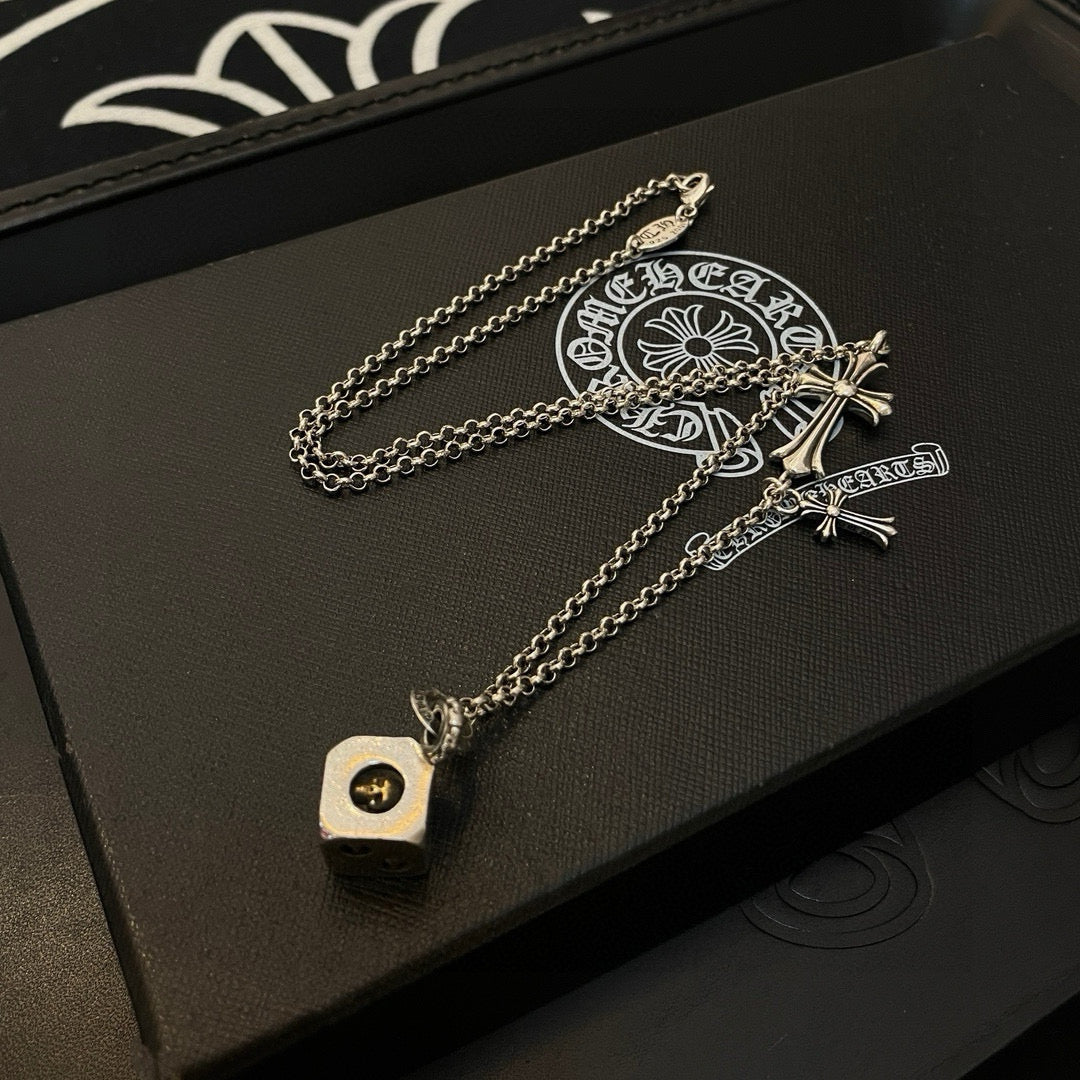 Silver charm necklace with cross charms and round logo pendant on a black box