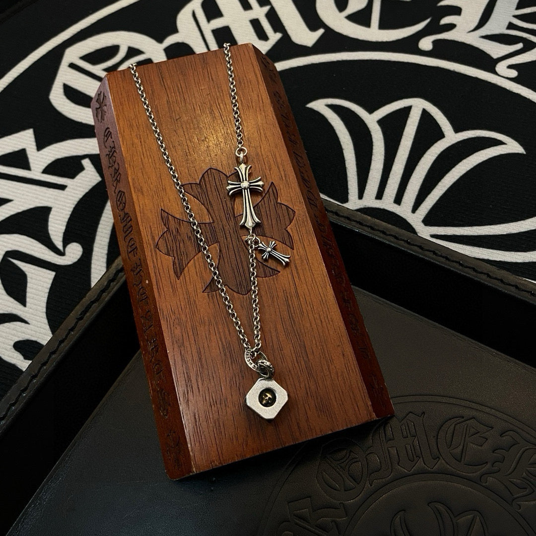 Silver charm necklace with cross charms and square coin pendant on a wooden block