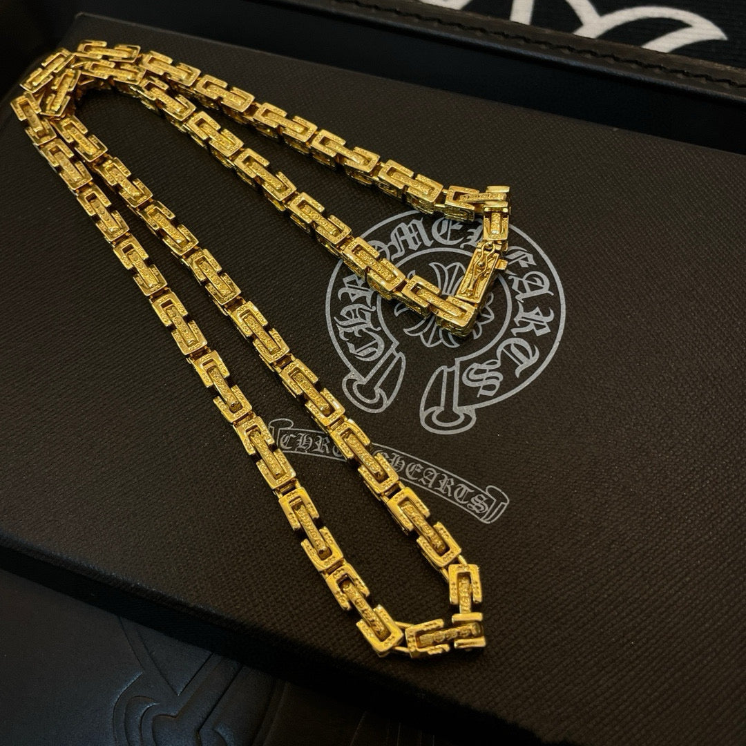 Gold tone chain necklace and bracelet on a black case, stacked rectangular links