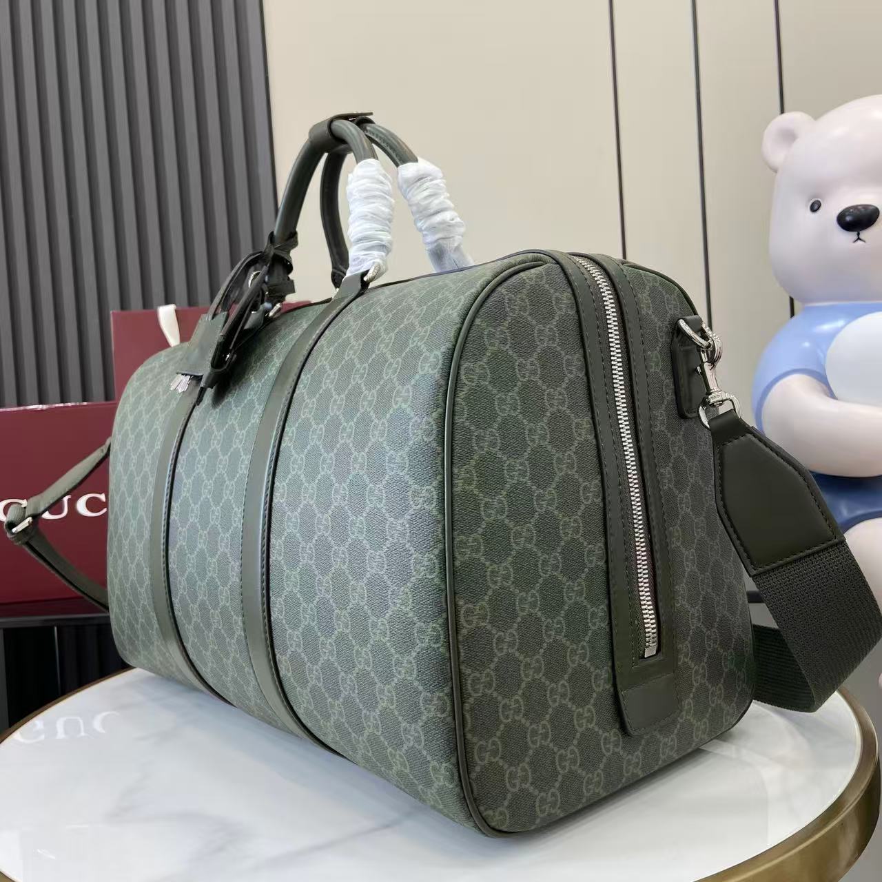 Gucci duffel bag angled view in dark green GG canvas with top handles and side zipper