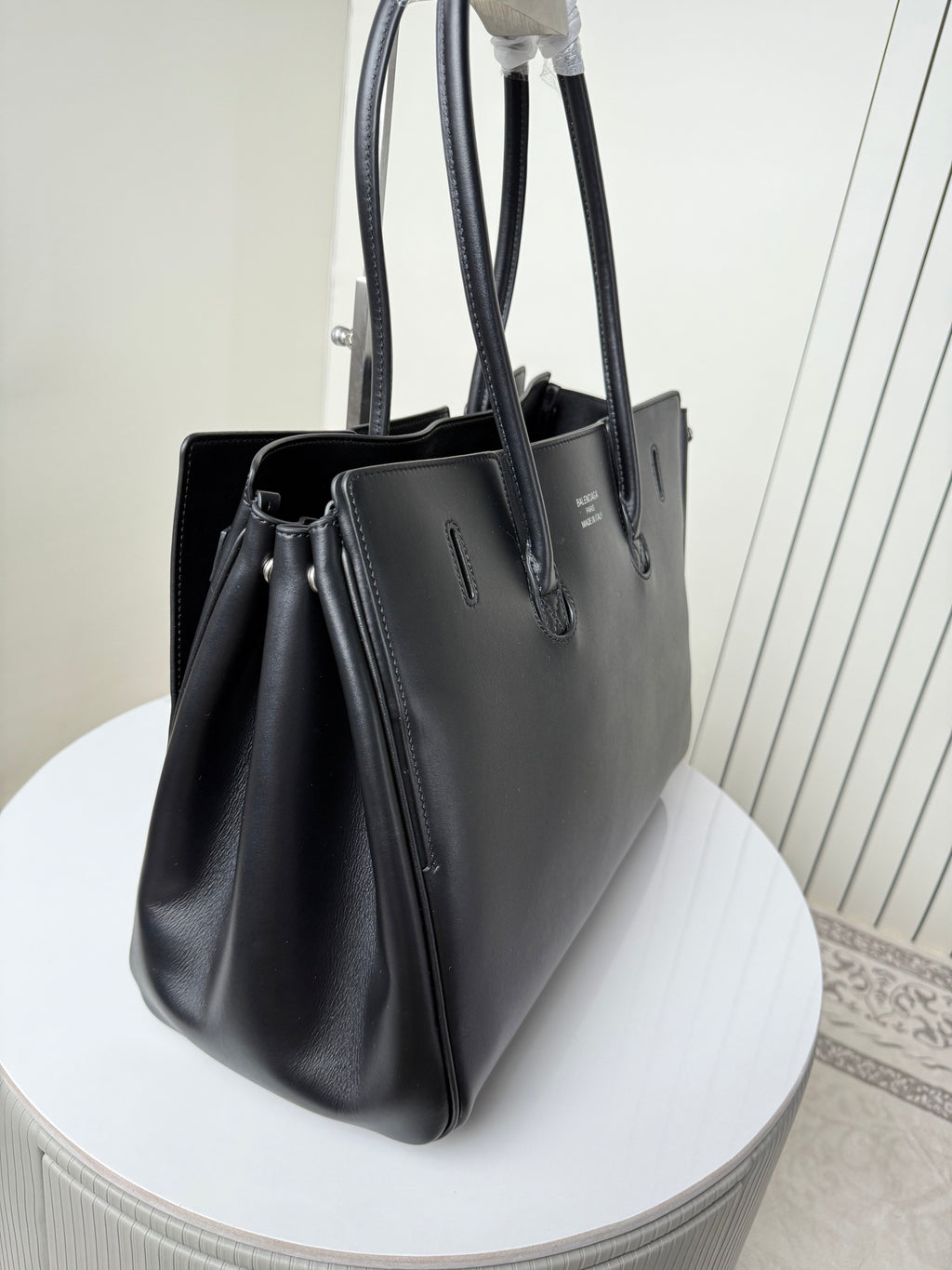 Black leather tote bag angled view with large handles and front charm
