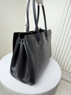 Black leather tote bag angled view with large handles and front charm