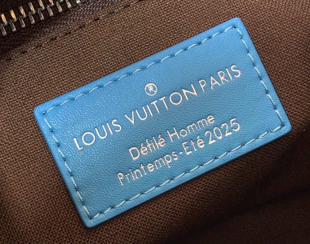 Blue leather logo tag on monogram handbag reading Louis Vuitton Paris Petite Homme