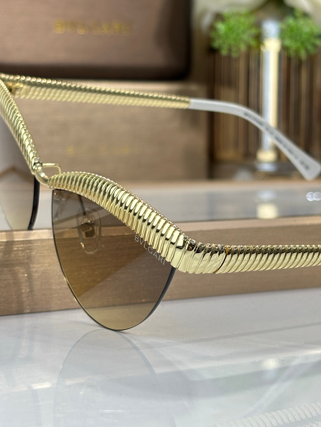 Bvlgari sunglasses close-up: gold textured metal temple and tinted round lens