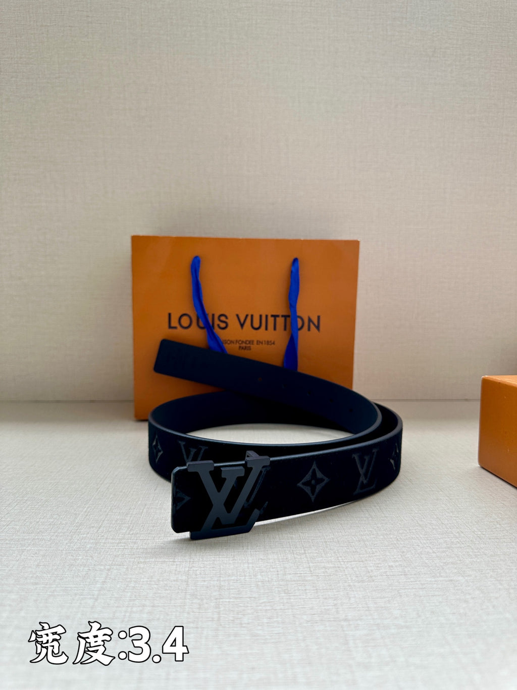 Leather belt with dark monogram strap and metal buckle, displayed on box