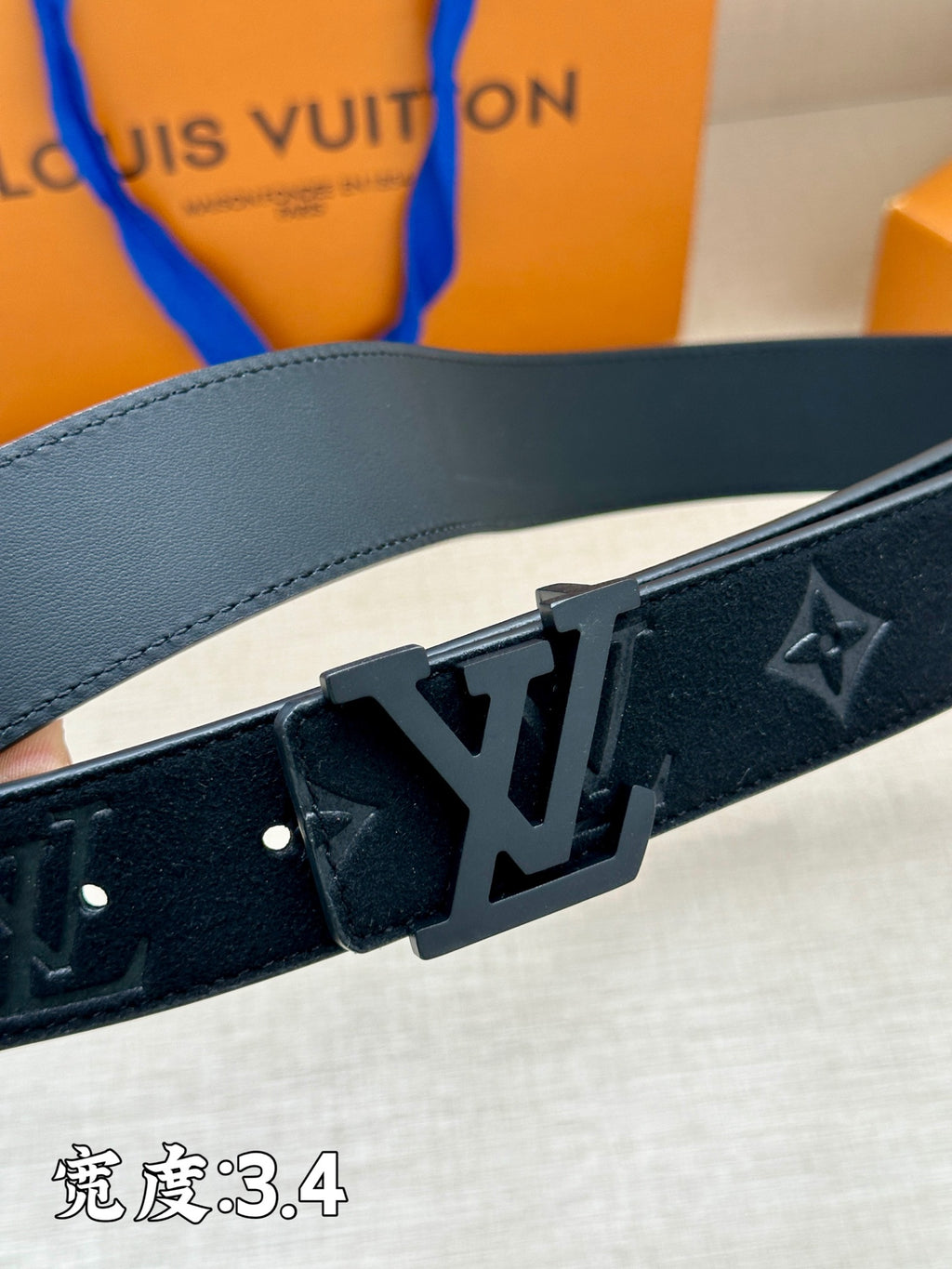 Leather belt close-up: dark monogram strap with metal buckle and studs