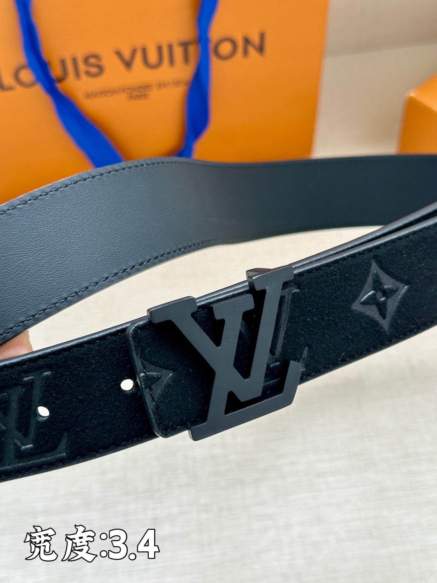 Leather belt close-up: dark monogram strap with metal buckle and studs