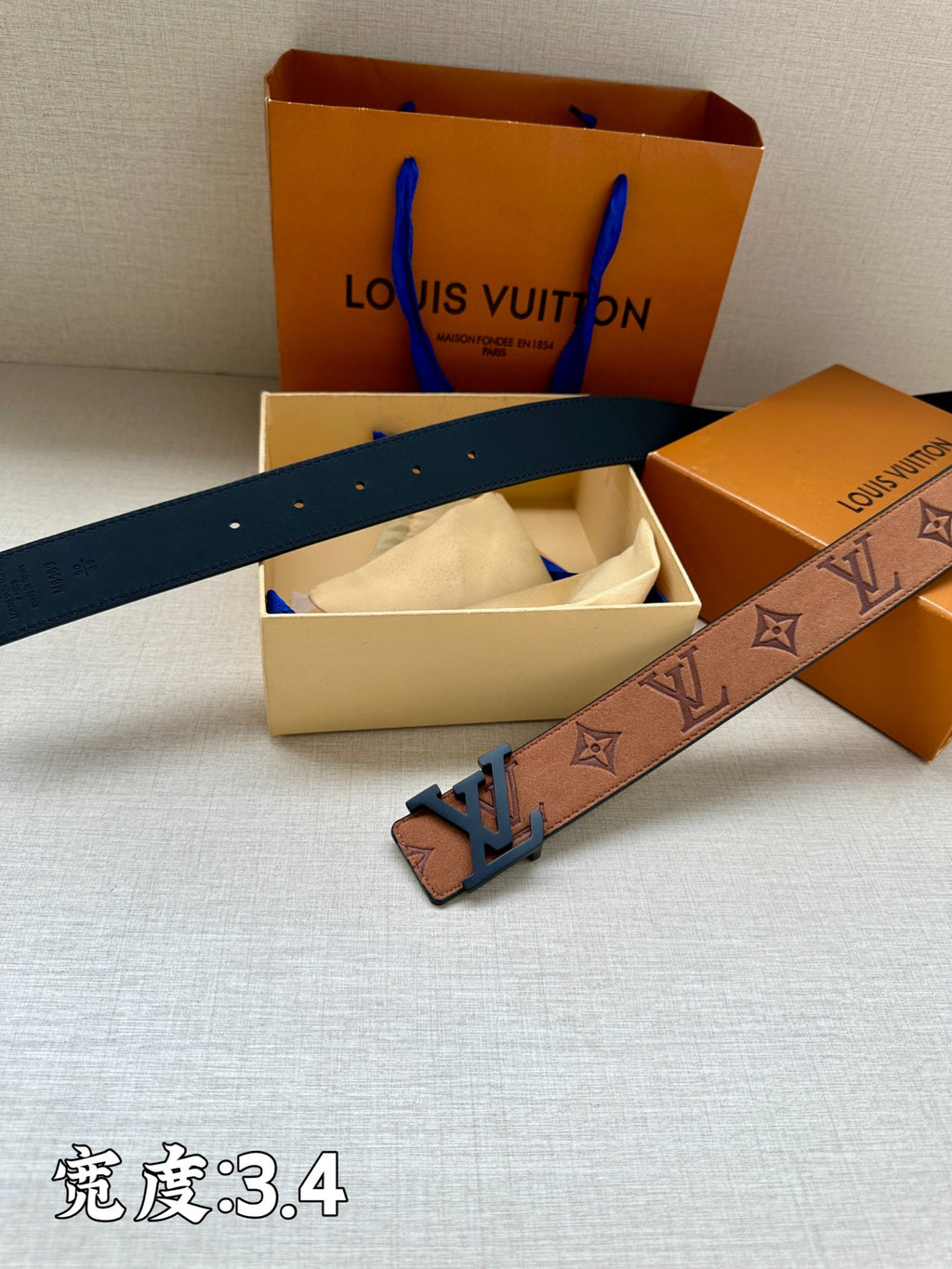 Tan monogram belt with dark blue LV buckle and punched holes, with boxes nearby