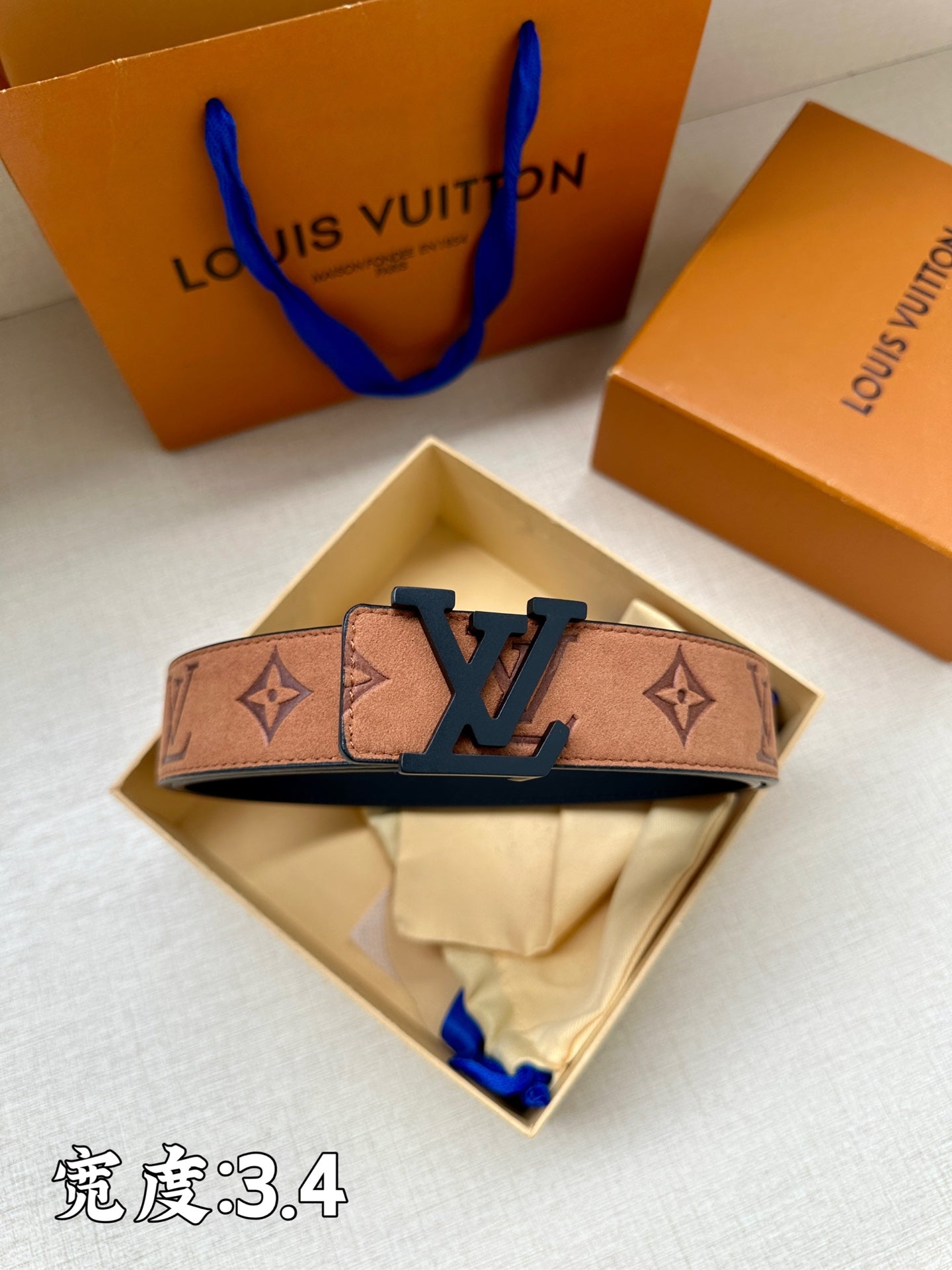 Tan monogram belt with dark blue LV buckle, shown in open box