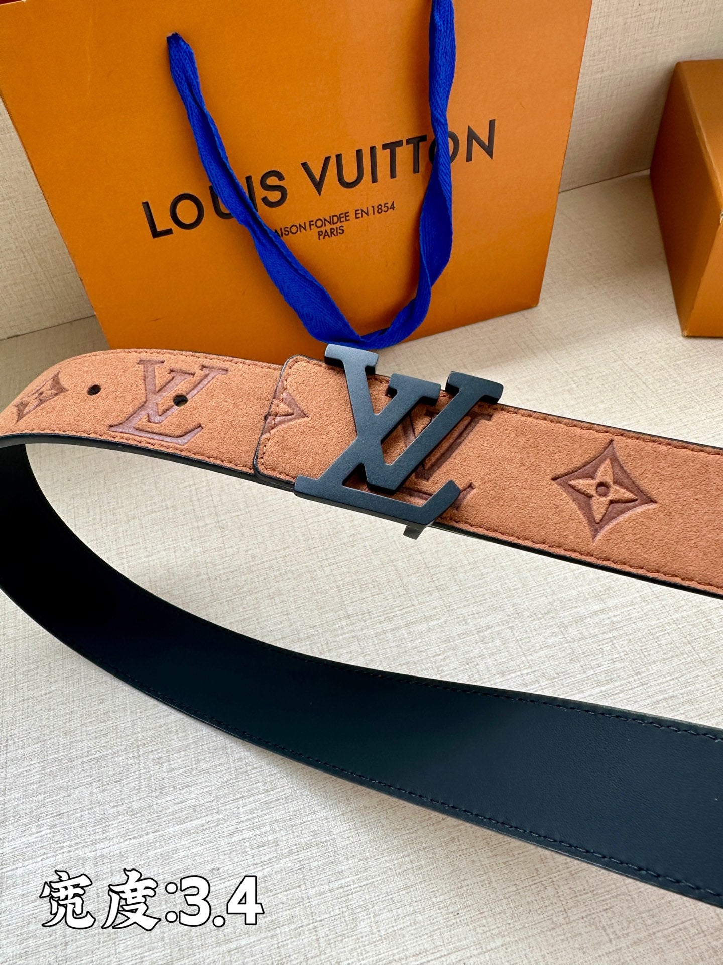 Tan monogram belt strap with dark blue LV buckle, close-up angled view